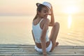 Beautiful sexual woman in white hat and bikini on a wooden pier against the sea and sunset Royalty Free Stock Photo