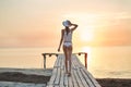 Beautiful sexual woman in white hat and bikini on a wooden pier against the sea and sunset Royalty Free Stock Photo