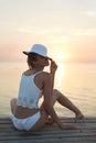 Beautiful sexual woman in white hat and bikini on a wooden pier against the sea and sunset Royalty Free Stock Photo