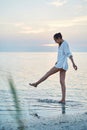 Beautiful sexual woman in white shirt and bikini walking on the beach against the sea and sunset Royalty Free Stock Photo