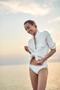 Beautiful sexual woman in white shirt and bikini walking on the beach against the sea and sunset Royalty Free Stock Photo