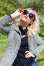 Beautiful blond girl with red lips in sunglasses walking in the garden of a bright sunny day Royalty Free Stock Photo
