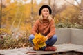 Beautiful sexy blonde in a brown warm sweater, black felt hat, blue jeans and boots sits on a bench in the autumn in the park, Royalty Free Stock Photo