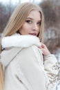 Beautiful blonde girl with long hair, full lips in a white coat walking in the winter woods