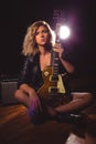 A beautiful and sexy blonde is sitting on a wooden floor and holding an electric guitar. Rear contour light and glare