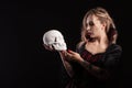 Beautiful and sexy blonde woman dressed up like a vampire holding and looking a skull Royalty Free Stock Photo