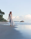 Beautiful, blonde woman walks at tropical beach, long dress