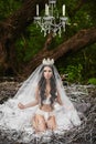 Beautiful and brunette model girl, in lingerie and crown, is sitting in a huge nest in the green forest Royalty Free Stock Photo
