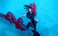 Beautiful sexy brunette young woman swimming with red cloths dress wrapped in clear turquoise blue pool water Royalty Free Stock Photo