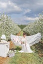 Beautiful cute girl in a light white dress in apple blossoming garden sees on the hammock with a book