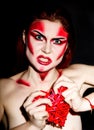 Beautiful devil girl with professional make-up. Fashion Art design. Attractive woman bites the heart Royalty Free Stock Photo