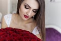 Beautiful devushkav white dressing gown with a large bouquet of red roses in a large bright room near the mirror Royalty Free Stock Photo