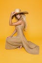 Beautiful, sexy, elegant woman with blond hair poses in studio in elegant yellow clothing and hat. Royalty Free Stock Photo