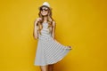 Beautiful and fashionable blonde model girl, in white stripe dress and hat and sunglasses, holds the bottom of her Royalty Free Stock Photo