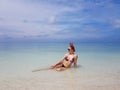 beautiful sexy fit woman in bikini and sunglasses sitting in blue water on beach. Female wearing christmas reindeer headband Royalty Free Stock Photo