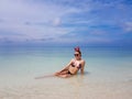 beautiful sexy fit woman in bikini and sunglasses sitting in blue water on beach. Female wearing christmas reindeer headband Royalty Free Stock Photo