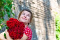 Beautiful and girl with a bouquet of red roses stands on the background of an old brick wall. Royalty Free Stock Photo