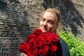 Beautiful and girl with a bouquet of red roses stands on the background of an old brick wall. Royalty Free Stock Photo