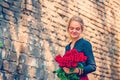 Beautiful and girl with a bouquet of red roses stands on the background of an old brick wall. Royalty Free Stock Photo