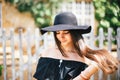 Beautiful girl brunette with brown eyes in a black dress and a black hat with big brims against the backdrop of a wooden fenc Royalty Free Stock Photo