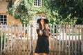 Beautiful girl brunette with brown eyes in a black dress and a black hat with big brims against the backdrop of a wooden fenc Royalty Free Stock Photo