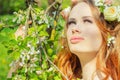 Beautiful girl with red hair with flowers in her hair stands near a blossoming Apple trees Royalty Free Stock Photo