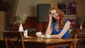 The beautiful sexy girl with red hair sitting in cafe, posing and smiling