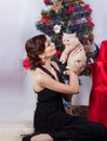 Beautiful happy smiling young woman in evening dress with bright makeup with red lipstick, sitting by the Christmas tree