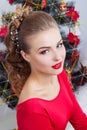 Beautiful happy smiling young woman in evening dress with bright makeup with red lipstick sitting near the Christmas tree Royalty Free Stock Photo