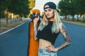 A beautiful, hipster blonde with blue hair in tattoo stands with a longboard Royalty Free Stock Photo