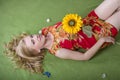 Beautiful blond young girl with sunflower in her hand posing lying on artificial grass Royalty Free Stock Photo