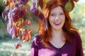 Beautiful lovely young foxy fiery red-haired girl, under violet lilac autumn bush, in the park, happy, cheerful,