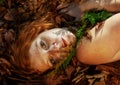 Beautiful sexy lovely young redhead girl lying on red golden autumn leaves, with a frond of fern on his chin, in the forest, with Royalty Free Stock Photo
