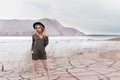 Beautiful slender girl in a black hat in the mountains with a strong wind