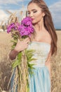 Beautiful slim girl in a blue dress in the field with a bouquet of flowers and ears of corn in his hands at sunset on a sunny Royalty Free Stock Photo