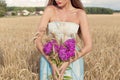 Beautiful slim girl in a blue dress in the field with a bouquet of flowers and ears of corn in his hands at sunset on a sunny Royalty Free Stock Photo