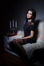 Beautiful sweet girl with full lips bright makeup sitting on the sofa with a glass of wine in a black evening dress