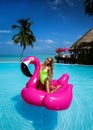 Beautiful sexy tanned woman on pink flamingo in pool. Young glamour girl in swimsuit on Maldives island. Perfect body bikini model Royalty Free Stock Photo