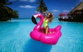 Beautiful sexy tanned woman on pink flamingo in pool. Young glamour girl in swimsuit on Maldives island. Perfect body bikini model Royalty Free Stock Photo