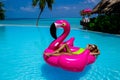 Beautiful sexy tanned woman on pink flamingo in pool. Young glamour girl in swimsuit on Maldives island. Perfect body bikini model Royalty Free Stock Photo