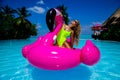 Beautiful sexy tanned woman on pink flamingo in pool. Young glamour girl in swimsuit on Maldives island. Perfect body bikini model Royalty Free Stock Photo