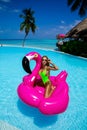 Beautiful sexy tanned woman on pink flamingo in pool. Young glamour girl in swimsuit on Maldives island. Perfect body bikini model Royalty Free Stock Photo