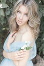 Beautiful tender blonde girl in blue light dress with a sprig of jasmine in his hands sitting the garden in the style Royalty Free Stock Photo