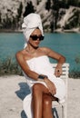 Beautiful sexy woman with dark hair with bath towels on body and head posing near lake and mountains Royalty Free Stock Photo