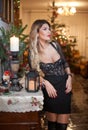 Beautiful woman in elegant black dress with Xmas tree in background. Portrait of fashionable blonde girl posing indoor Royalty Free Stock Photo