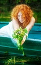 Beautiful sexy woman with red hair, bride, Lady of Shalott, with a bouquet of flowers in a boat Royalty Free Stock Photo