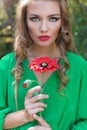 Beautiful woman with red lips and bright make-up in a green dress with a poppy in his hands in a forest Royalty Free Stock Photo