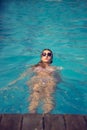 Beautiful woman swimming backside in a perfect blue water wearing sunglasses