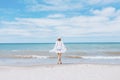 Beautiful sexy woman wearing straw hat, white swimsuit and skirt walking along the surf line on beach. Summer holidays in tropics Royalty Free Stock Photo