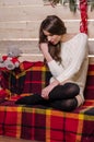 Beautiful sexy woman with Xmas tree in background sitting on elegant chair in cozy scenery. Portrait of girl posing Royalty Free Stock Photo